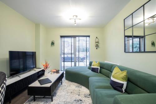 a living room with a green couch and a flat screen tv at Elliot Oliver - Deluxe Two Bedroom Apartment With Parking & EV Charger in Cheltenham