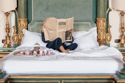 a woman laying on a bed reading a newspaper at La Posta Vecchia Hotel in Ladispoli