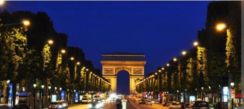 a lit up street with a large arch at night at Arc de triomphe studio charme authentique in Paris