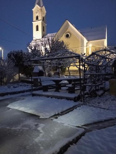 a church with a bench in the snow at night at Guesthouse Pavličić in Drežnik Grad