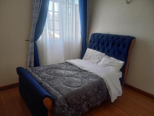 a bed with a blue headboard and a window at Amreff Nyumbani villas in Kitengela 
