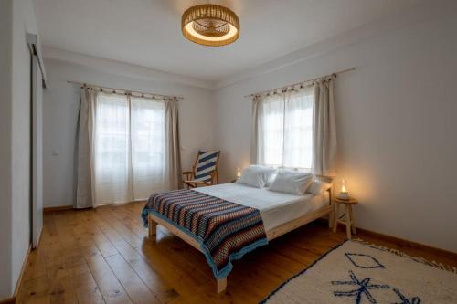 a bedroom with a bed with a rug and two windows at Apartamento Aires - Trafaria in Trafaria