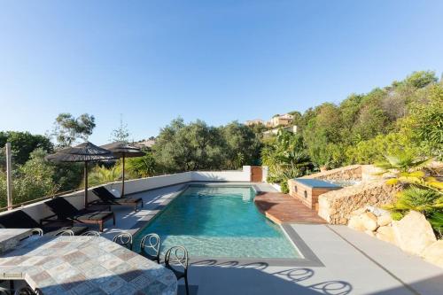 une piscine avec deux chaises et un parasol dans l'établissement Villa d'architecte, piscine et jacuzzi, à quelques mètres de la plage, à Pietrosella