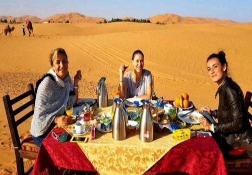 three women sitting at a table in the desert at Desert Berber Fire Camp in Merzouga