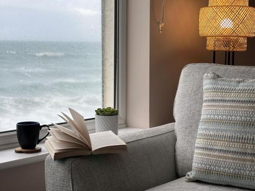 a book sitting on a chair in front of a window at Aggie Beach Apartment - Unrivalled Beach Views in St. Agnes