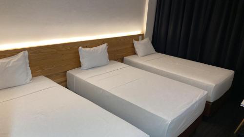 three beds in a room with white sheets and pillows at Executive Inn Fernandopolis in Fernandópolis
