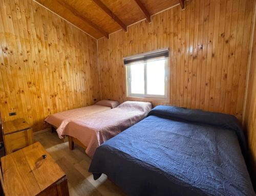 Cette chambre en bois dispose de 2 lits et d'une fenêtre. dans l'établissement Cabaña Melipeuco, à Melipeuco
