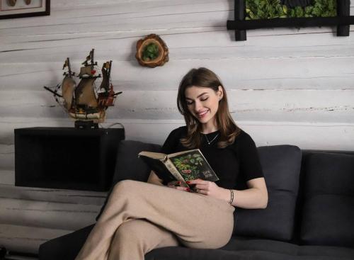 une femme assise sur un canapé qui lit un livre dans l'établissement База відпочинку Forest Stream, à Svalyava