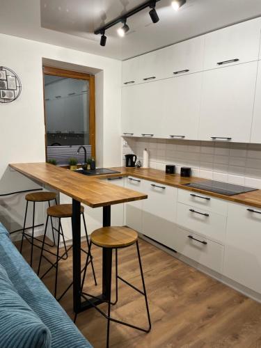a kitchen with white cabinets and a wooden table with stools at Apartament 61 " W Chmurach" in Toruń