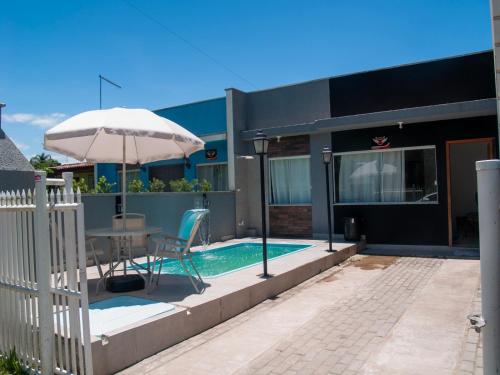 una casa con una mesa y una sombrilla junto a una piscina en Cada com piscina 50mts da praia!, en Itapoa