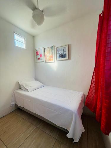 a small bedroom with a white bed and red curtains at Mini Casa Vista Mar in Salvador