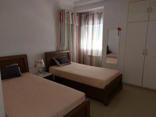1 Schlafzimmer mit 2 Betten und einem Fenster mit Vorhängen in der Unterkunft Résidence Sayadi - Chatt Meriam - Sousse in Port El-Kantaoui