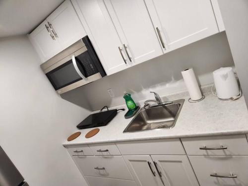 a white kitchen with a sink and a microwave at A Modern & Homely 1 BR Suite in Winnipeg
