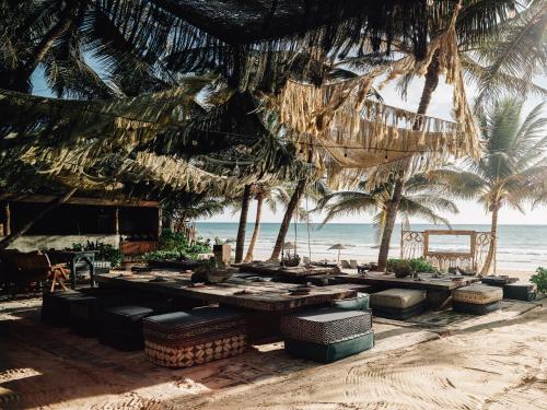 a beach with tables and palm trees and the ocean at Nômade Temple Tulum in Tulum