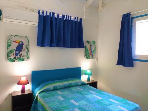 1 dormitorio con cama azul y cortinas azules en Résidence les Océanides, en Le Diamant
