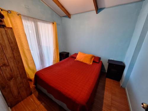 a small bedroom with a red bed with a window at Cabañas puna poho in Hanga Roa