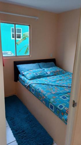 a bed with a blue comforter and a window at Dushi Curaçaose appartement in Willemstad