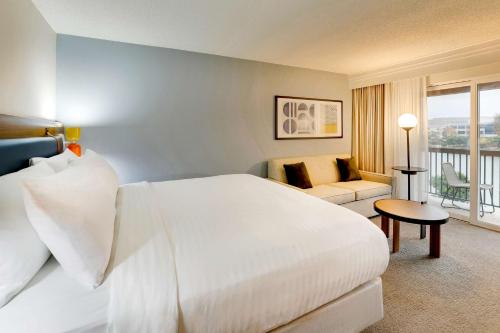 a bedroom with a large white bed and a living room at Sonesta Select San Francisco Airport Oyster Point Waterfront in South San Francisco