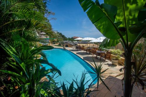 a swimming pool with plants and tables and umbrellas at Pousada e Spa Villa Mercedes by Latitud Hoteles in Búzios