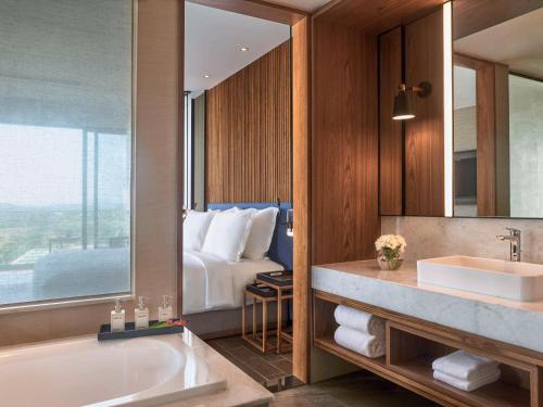 a bathroom with a tub and a sink and a bed at Mövenpick Resort Waverly Phu Quoc in Phu Quoc