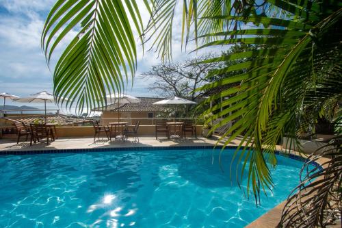 a pool with chairs and tables and a palm tree at Pousada e Spa Villa Mercedes by Latitud Hoteles in Búzios