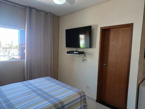 1 dormitorio con 1 cama y TV en la pared en Casa mar sol e piscina, en Peruíbe