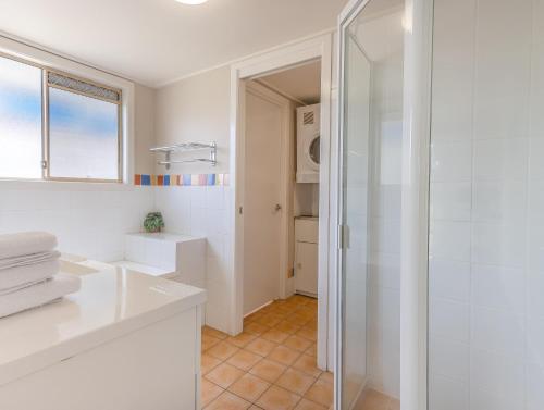 a white bathroom with a shower and a glass door at Hastings Cove Holiday Apartments in Hastings Point