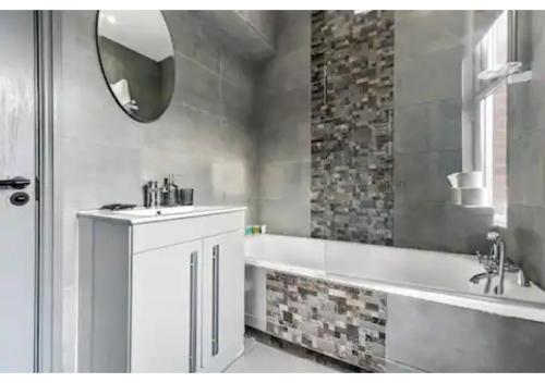 ein Badezimmer mit einer Badewanne, einem Waschbecken und einem Spiegel in der Unterkunft Three Bedroom Home - Perfect for Large Groups in London