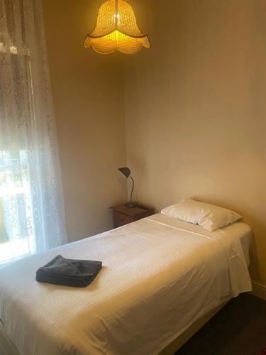 Commercial Hotel Camperdown في كامبرداون: غرفة نوم بسرير ابيض ومصباح ونافذة