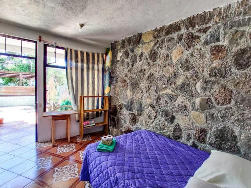 a bedroom with a purple bed and a stone wall at Casa Don Clemente in San Pedro La Laguna