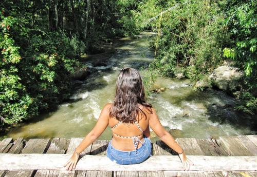 Eine Frau, die auf einer Brücke sitzt und einen Fluss ansieht. in der Unterkunft Ali Atrás in Macaé