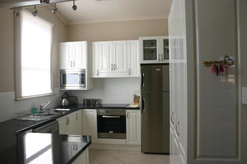 a kitchen with white cabinets and a stainless steel refrigerator at Primrose Cottage in Albury