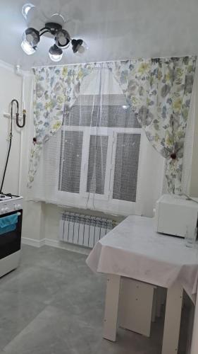 a kitchen with a table and a window with curtains at Парни in Qyzylorda