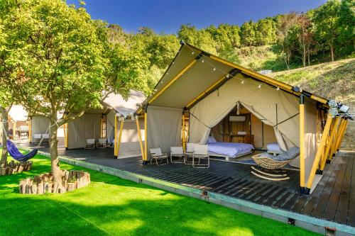 a luxury tent with a hammock on a deck at 山上種樹 l 苗栗豪華懶人露營Glamping l 柴燒泡湯 l 可包區森林系狩獵帳 l 牛樟森林休閒農場 in Miaoli