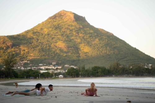 three people laying on a beach with a mountain in the background at Tamarina Golf & Spa Boutique Hotel in Flic-en-Flac