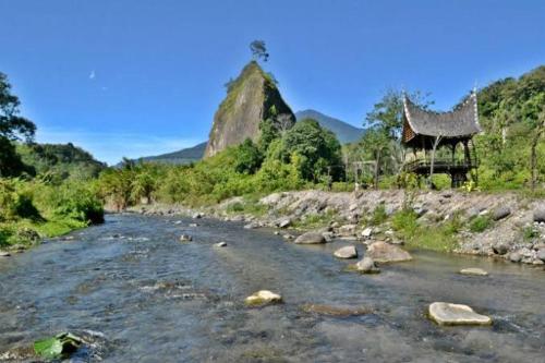 a river with rocks and a building in the background at Exorcism Camp in Bukittinggi