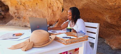 a woman sitting at a table with a laptop at Cave Diani Holiday Apartments in Diani Beach