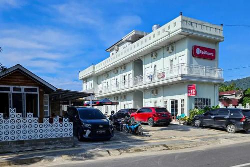 a white building with cars parked in front of it at RedDoorz Syariah near Kantor Bupati Pantai Pandan Sibolga in Halangan