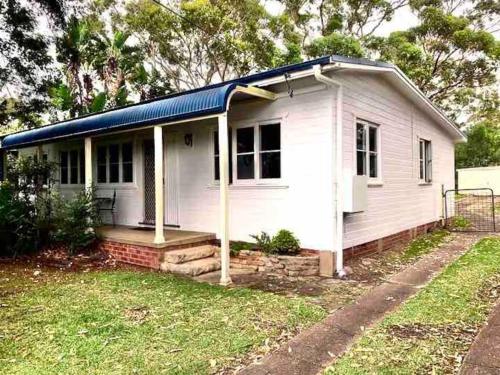 a white house with a blue roof and a yard at Cosy two bedroom bungalow close to lake and ocean in Berrara
