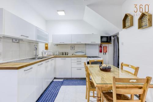 een keuken met witte kasten en een houten tafel en stoelen bij Peaceful 1BR maisonette with Sofa Bed with WIFI by 360 Estates in St Paul's Bay