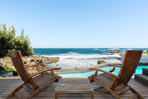 two chairs sitting on a deck next to a swimming pool at Sea Haven - Bakoven Beach Front Villa in Cape Town