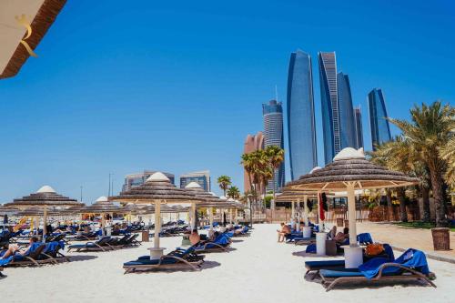 a beach with many chairs and umbrellas and buildings at Beach bliss 3BR apartment Corniche in Abu Dhabi