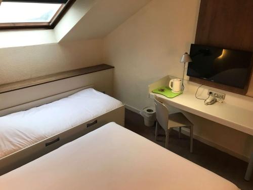 a room with a bed and a desk with a television at Campanile Lille Nord Wasquehal in Wasquehal