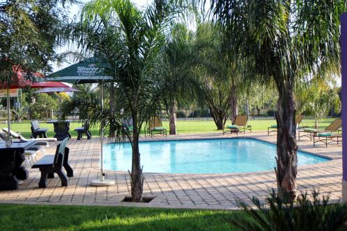uma piscina num parque com árvores e mesas em Casa Bianca Guest Lodge em Hartbeespoort