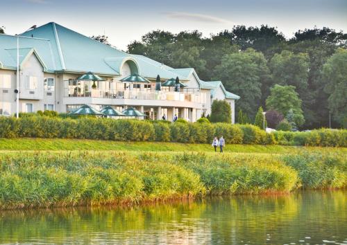 a couple standing in front of a large building next to a lake at Hotel HP Park Poznań Malta in Poznań