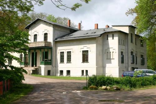 een oud wit huis met een auto voor de deur bij Gutshaus Bartelshagen 