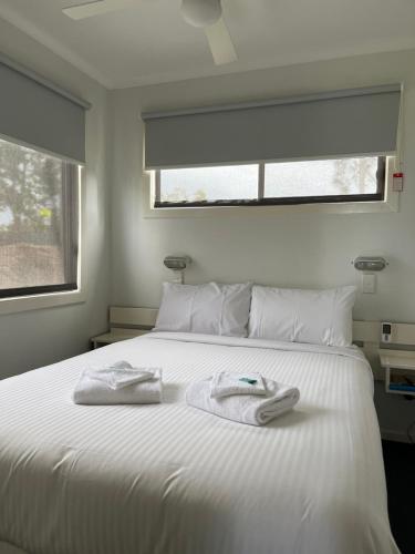 una camera da letto con un letto bianco e asciugamani di Diamond Beach Holiday Park a Diamond Beach