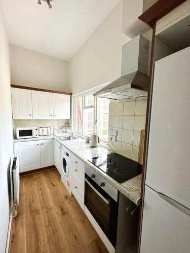 cocina con armarios blancos y nevera negra en Centrally located studio flat sleeps 4, en Ealing