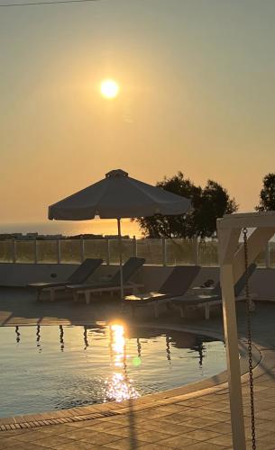 an umbrella and chairs next to a pool with the sunset at Maria's Place - Adults Only in Oia