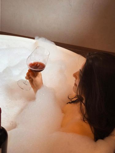 a woman in a bath tub holding a glass of wine at Chalés Vani in Resende